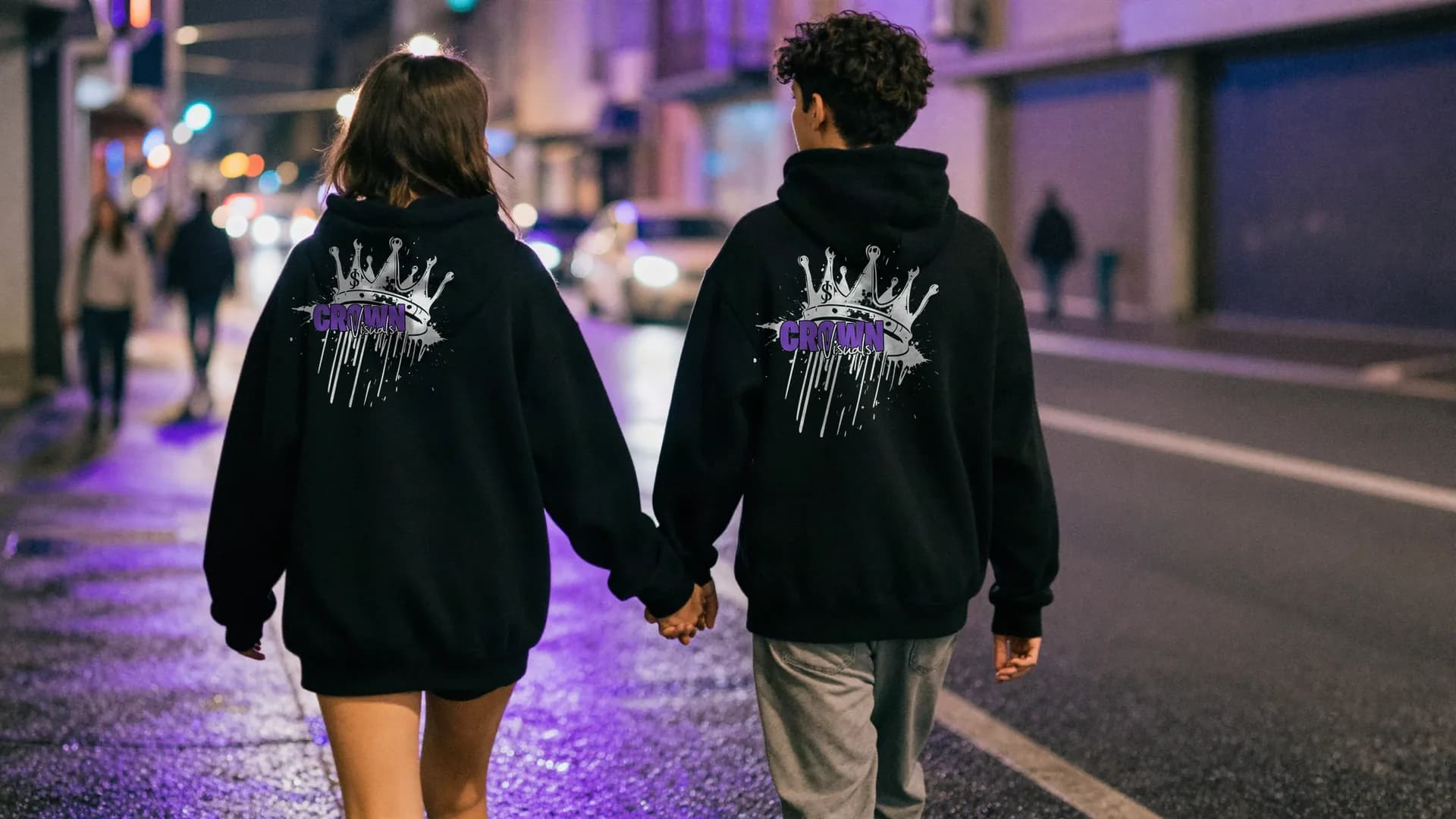 Paar von hinten in schwarzen Crown-Visuals-Hoodies auf einer nächtlichen Straße